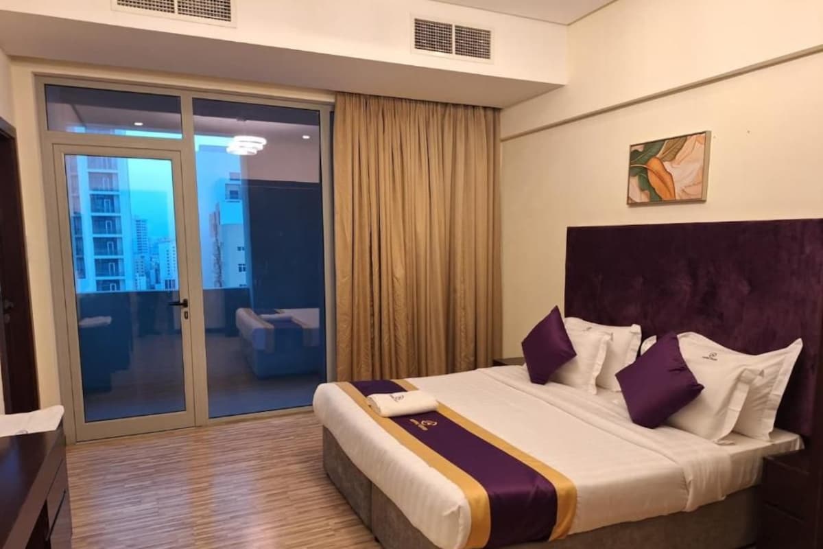 A hotel room with a bed, a sliding door to a balcony, and a painting on the wall.