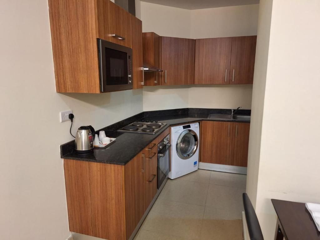 Cozinha compacta com armários de madeira, micro-ondas, fogão e máquina de lavar.