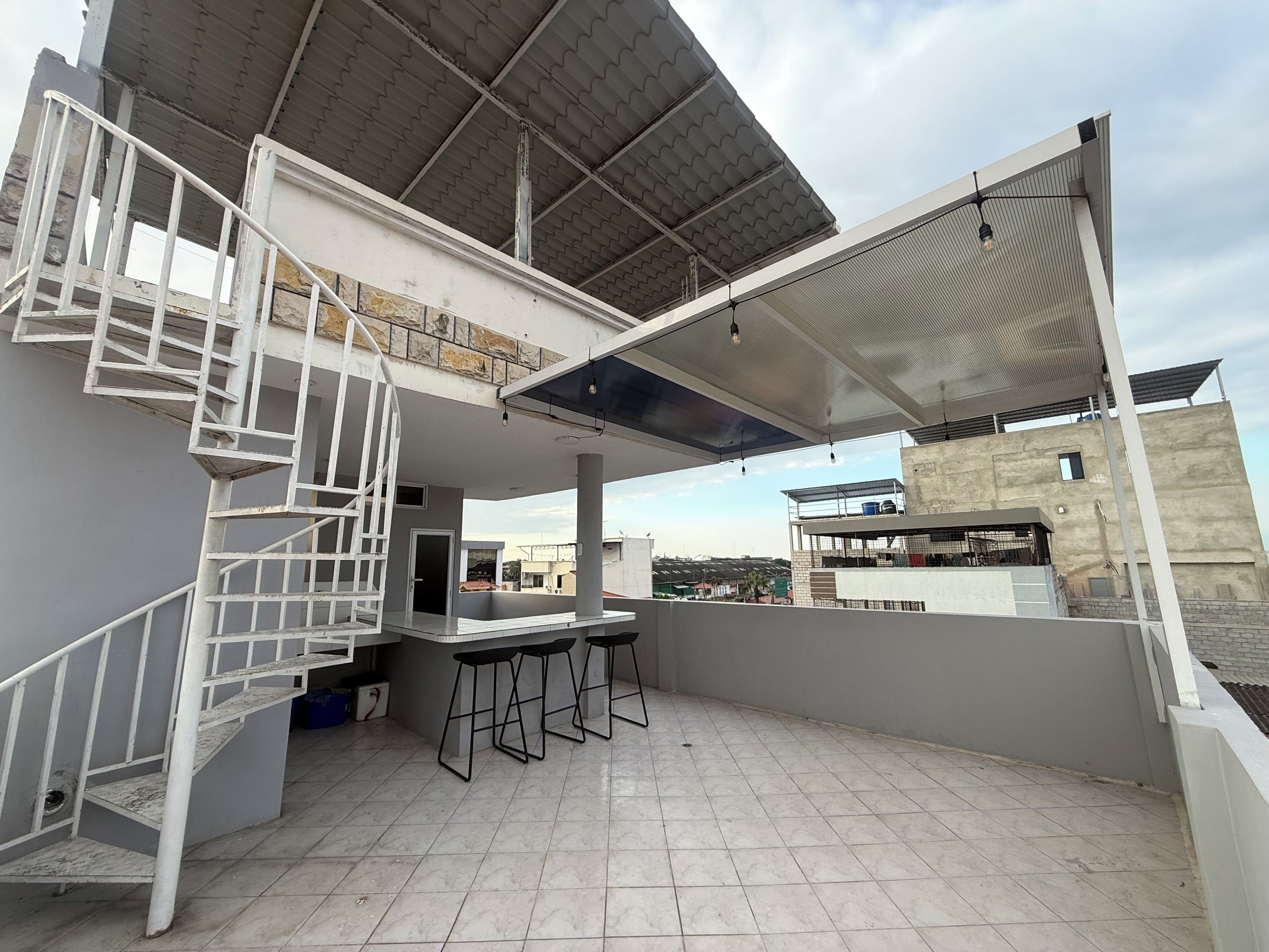 Eine Dachterrasse mit weißer Wendeltreppe, einer Bar mit Hockern und einem überdachten Sitzbereich.