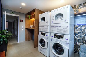 A laundry facility with multiple washing machines, a wooden shelf with toiletries, and a sign indicating a first-floor location. - New Listing (São Paulo)