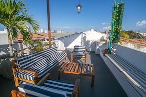 Eine Dachterrasse mit Blick auf die Stadtlandschaft, inklusive einem Holztisch und zwei gestreiften Liegestühlen.