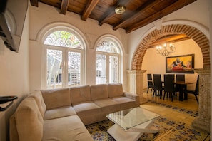 Ein Wohnzimmer mit einem beigen Sofa, einem Glastisch und einem Essbereich mit Tisch und Stühlen.