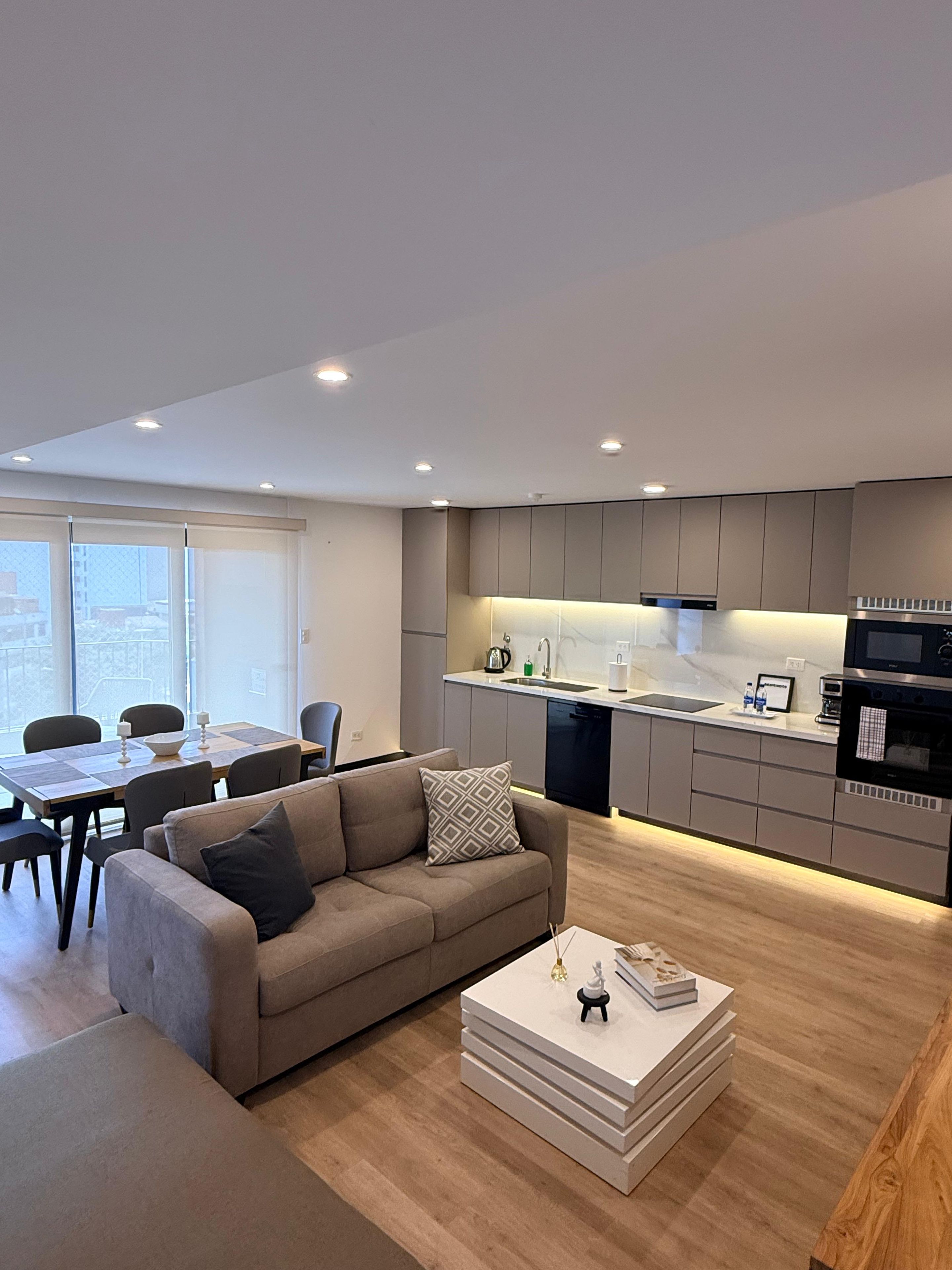 A modern living space with a sofa, dining table, and kitchen area.