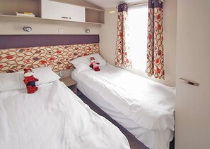 Een hotelkamer met twee eenpersoonsbedden, een klein nachtkastje, een kledingkast en een raam met gordijnen met een patroon.