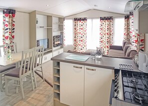 A compact kitchen with a gas stove, a dining area with chairs, and a small table. - New in 2017. 12ft-wide caravan with one double and two twin. (St. Leonards, Ringwood)
