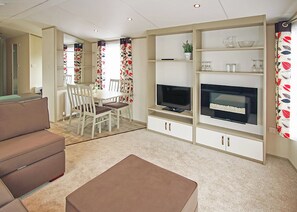 A modern living room with a flat-screen TV, a sofa, a dining table, and a coffee table. - New in 2017. 12ft-wide caravan with one double and two twin. (St. Leonards, Ringwood)