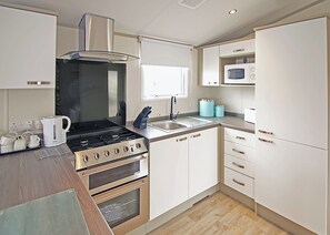 A compact kitchen with a gas stove, oven, microwave, and white cabinetry. - New in 2017. 12ft-wide caravan with one double and two twin. (St. Leonards, Ringwood)
