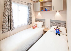 Et soveværelse med to senge, et vindue med gardiner, en hylde med toiletartikler og en sengegavl med et zig-zag mønster.