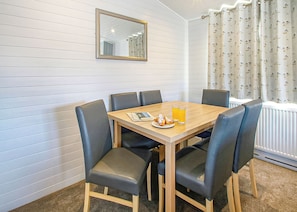 A dining area with a wooden table, six chairs, a mirror, and a window with curtains. - Select Lodge Plus 2 (Pet) (Milford-on-Sea, Nr Lymington)