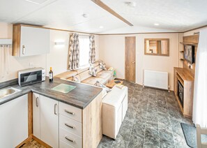 A compact kitchen with a microwave, a wine bottle, and a dining area with a sofa and a table. - New in 2017. Luxury 12ft-wide caravan. (Milford-on-Sea, Nr Lymington)