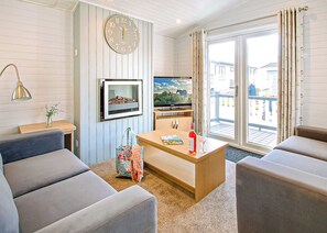 A modern living room with a sofa, a coffee table, a television, and a clock on the wall. - Superior Lodge Plus 4 (Pet) (Milford-on-Sea, Nr Lymington)