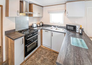 A compact kitchen with a gas stove, oven, microwave, and a sink. - New in 2017. Luxury 12ft-wide caravan. (Milford-on-Sea, Nr Lymington)