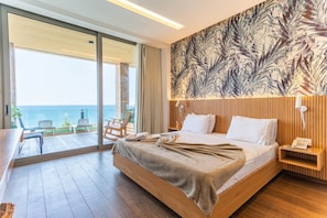 A hotel room with a large bed, a wooden headboard, a view of the sea, and a balcony with outdoor seating. - Feghalo Fghal by Stayinn (Fghal)