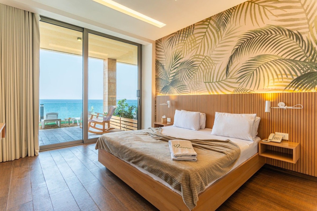 A hotel room with a large bed, a wooden headboard, a view of the ocean, a wooden nightstand, and a telephone.