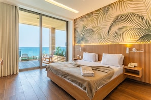 A hotel room with a large bed, a wooden headboard, a view of the ocean, a wooden nightstand, and a telephone. - Feghalo Fghal by Stayinn (Fghal)