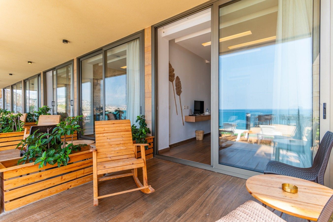 A modern interior with a wooden bench, a small table, and a view of the ocean through large glass doors.