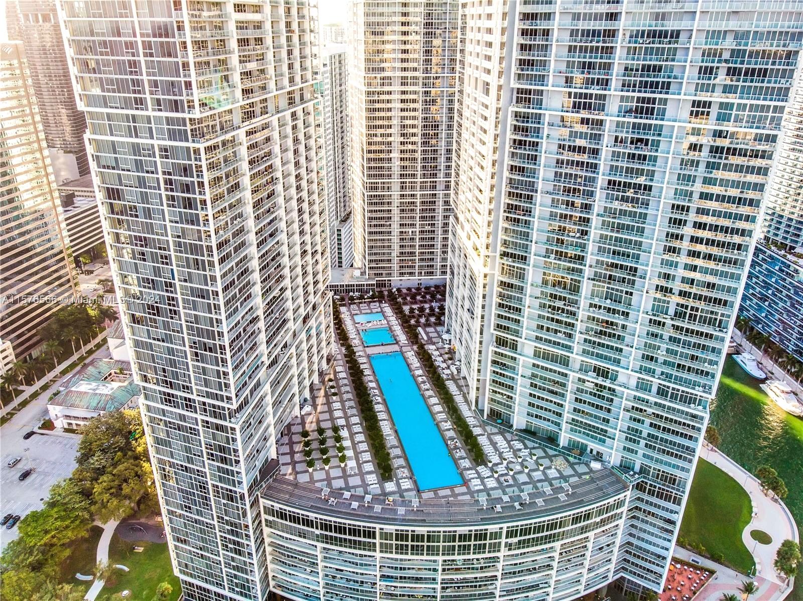A high-rise building with a central courtyard featuring a swimming pool, surrounded by other high-rise buildings.