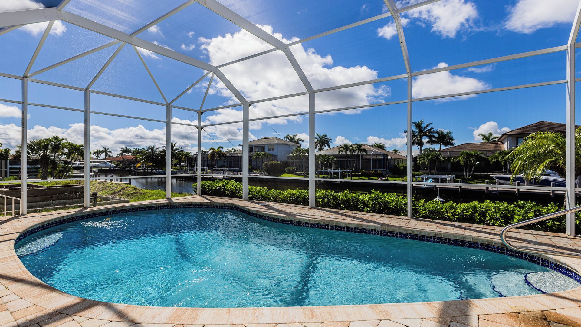 A swimming pool with a clear blue water, surrounded by a covered area with a metal frame and glass panels.