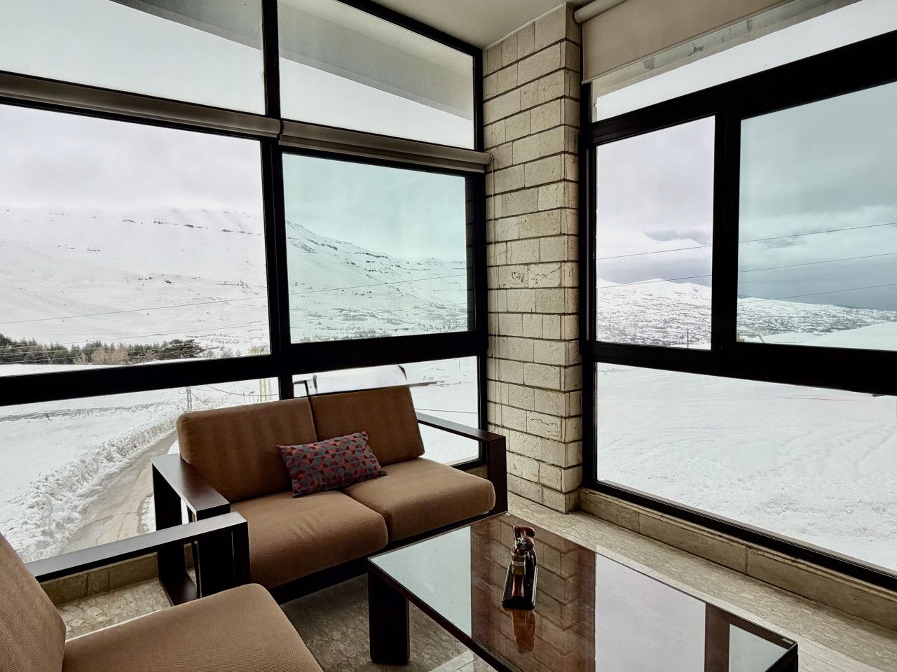 A modern living room with a sofa and coffee table, large windows with a snowy landscape view.