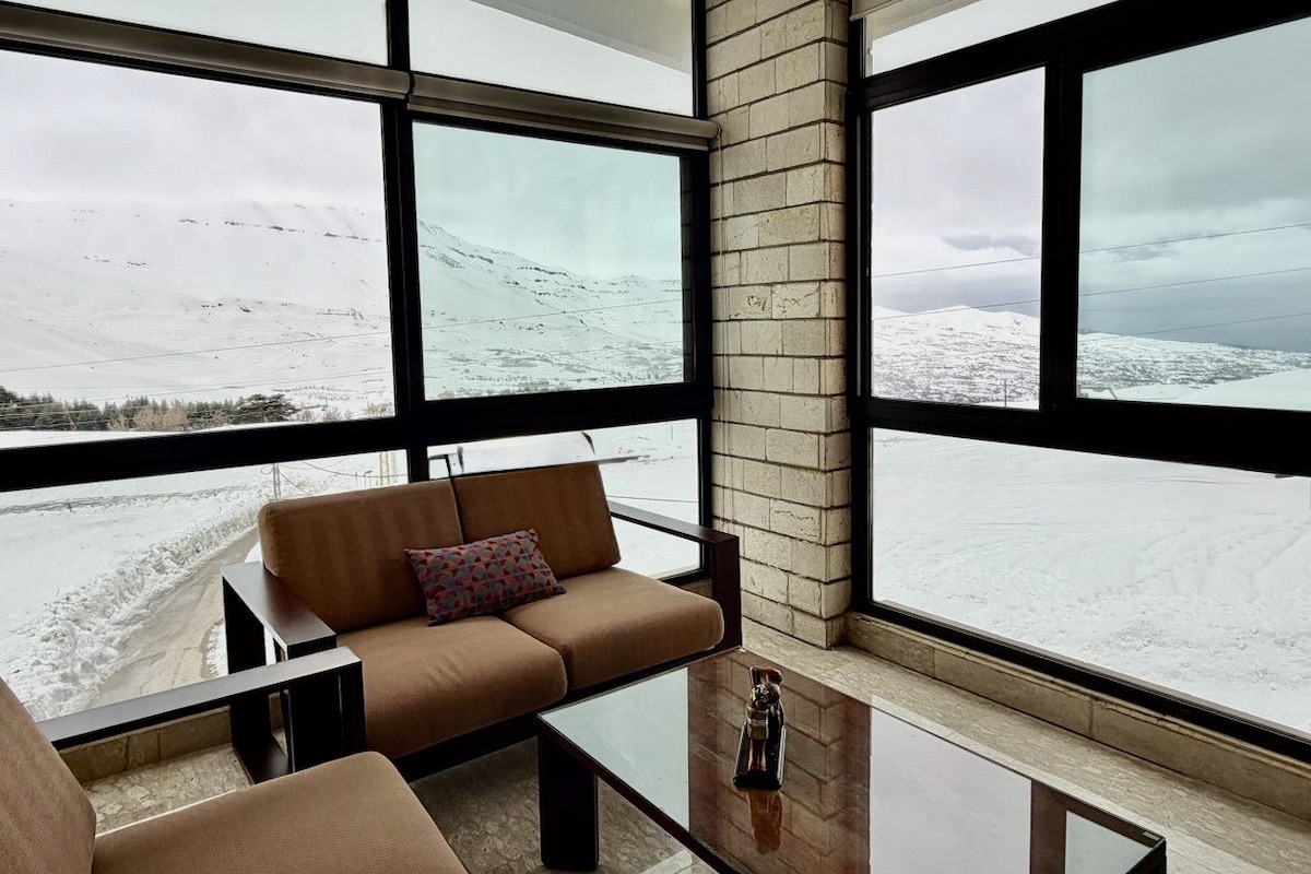 Ein modernes Wohnzimmer mit Sofa und Couchtisch, große Fenster mit Blick auf eine verschneite Landschaft.