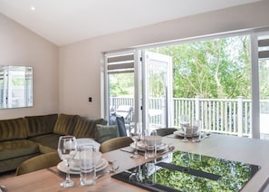 A modern living room with a sofa, dining table set with glasses and plates, and a view of greenery through large windows. - 1 bedroom accommodation in Doncaster, South Yorkshire (Doncaster, South Yorkshire)