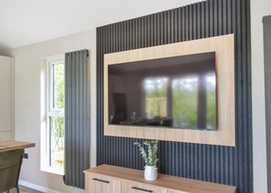 A modern living room with a built-in TV, a wooden cabinet below, and a window with curtains. - Buckingham Accessible (Doncaster, South Yorkshire)