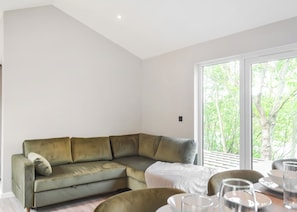 A modern living room with a sectional sofa, a dining table with chairs, and a large window with a view of trees. - Buckingham Accessible (Doncaster, South Yorkshire)