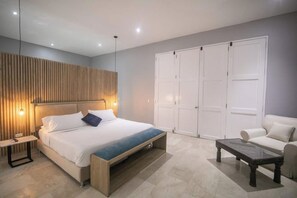 Quarto moderno com cama, mesas de cabeceira, um banco, um sofá e um guarda-roupa.