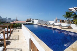 Piscina no terraço com espreguiçadeiras e vista para o horizonte da cidade.