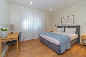 Een slaapkamer met een bed, een bureau, een stoel, een nachtkastje en een wandlamp.