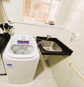 A compact washer and dryer unit with a small sink and a window above it. - Apto Térreo até 6 Pessoas Aeroporto  (Várzea Grande)