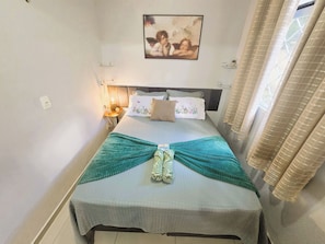 A neatly made bed with a patterned bedspread, a decorative pillow, and a wall-mounted picture. - Apto Térreo até 6 Pessoas Aeroporto  (Várzea Grande)