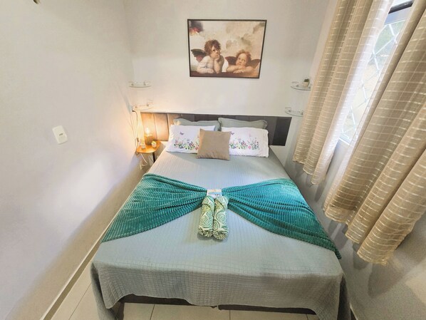 A neatly made bed with a patterned bedspread, a decorative pillow, and a wall-mounted picture.