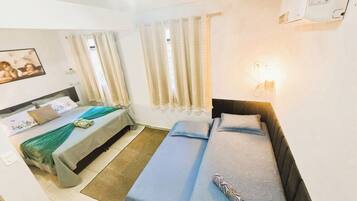 A hotel room with two beds, a bedside table, a lamp, and a wall-mounted power outlet.