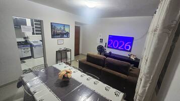 A living room with a TV displaying '2026', a dining table with a floral centerpiece, and a sofa.