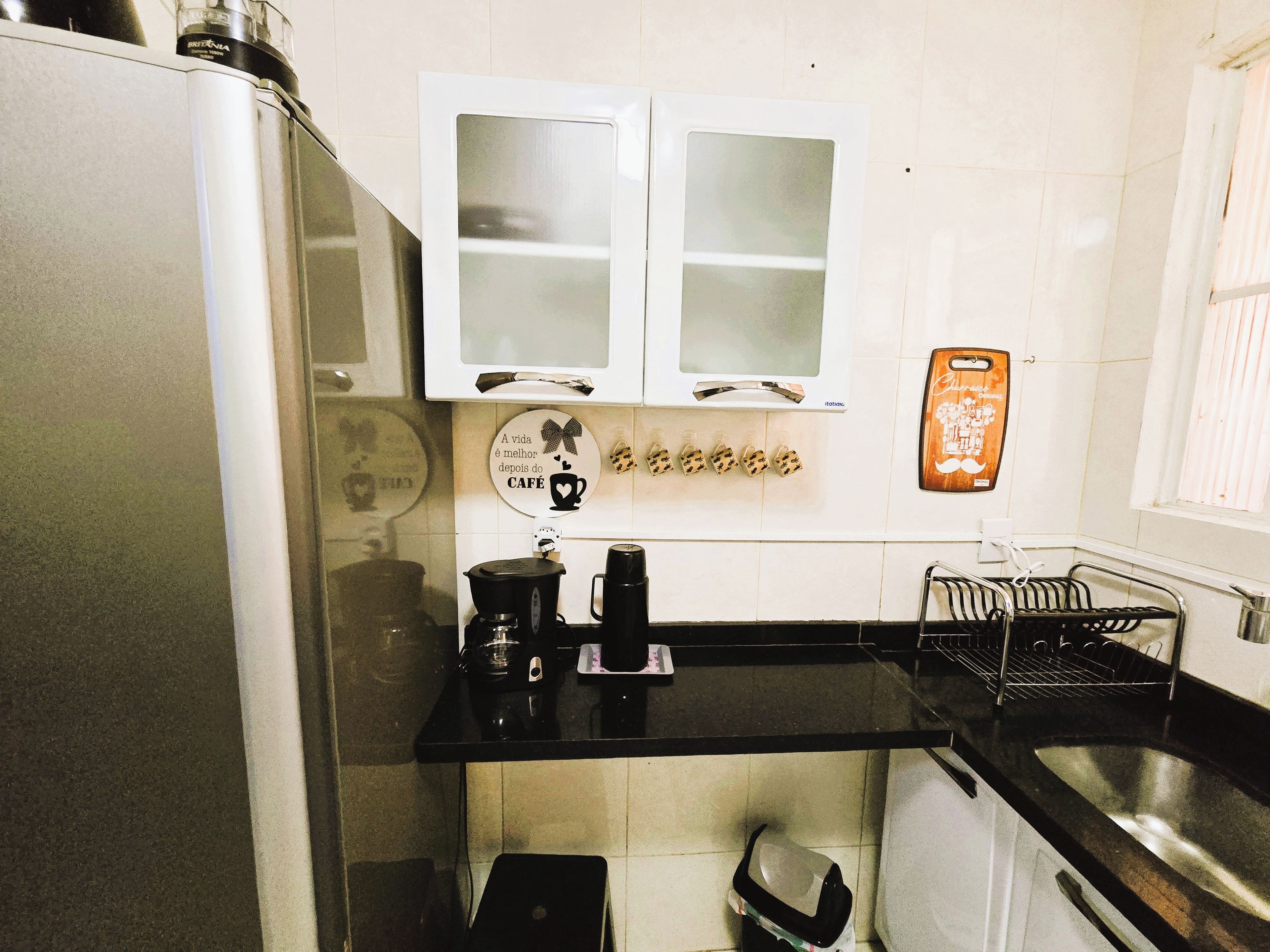 Cocina pequeña con armarios blancos, encimera negra y cafetera.