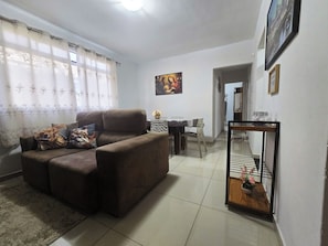 A living room with a sofa, a dining table, and a painting on the wall. - Apto Térreo até 6 Pessoas Aeroporto  (Várzea Grande)