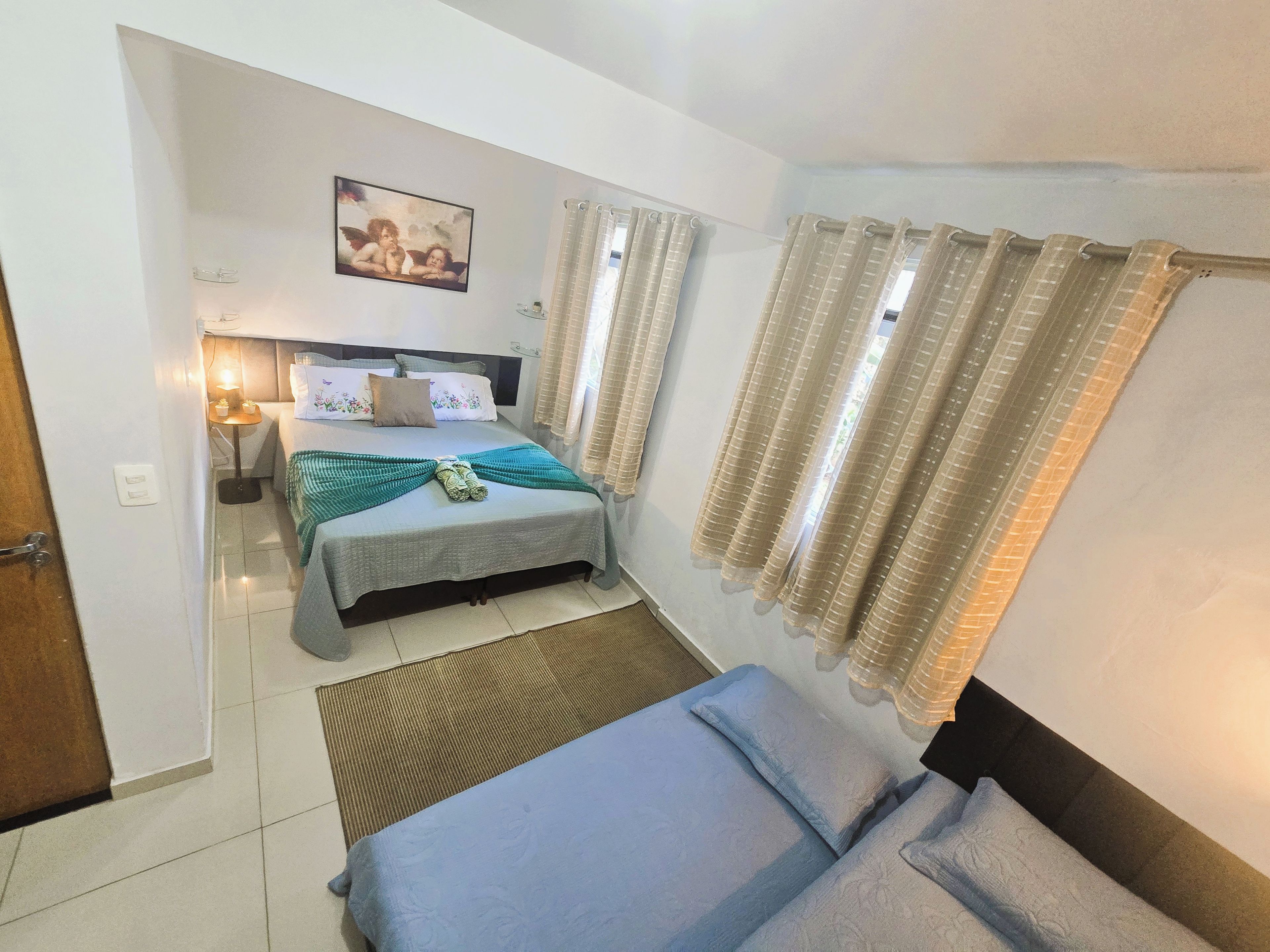 Una habitación de hotel con una cama, una mesita de noche, una lámpara, una ventana con cortinas y un cuadro colgado en la pared.