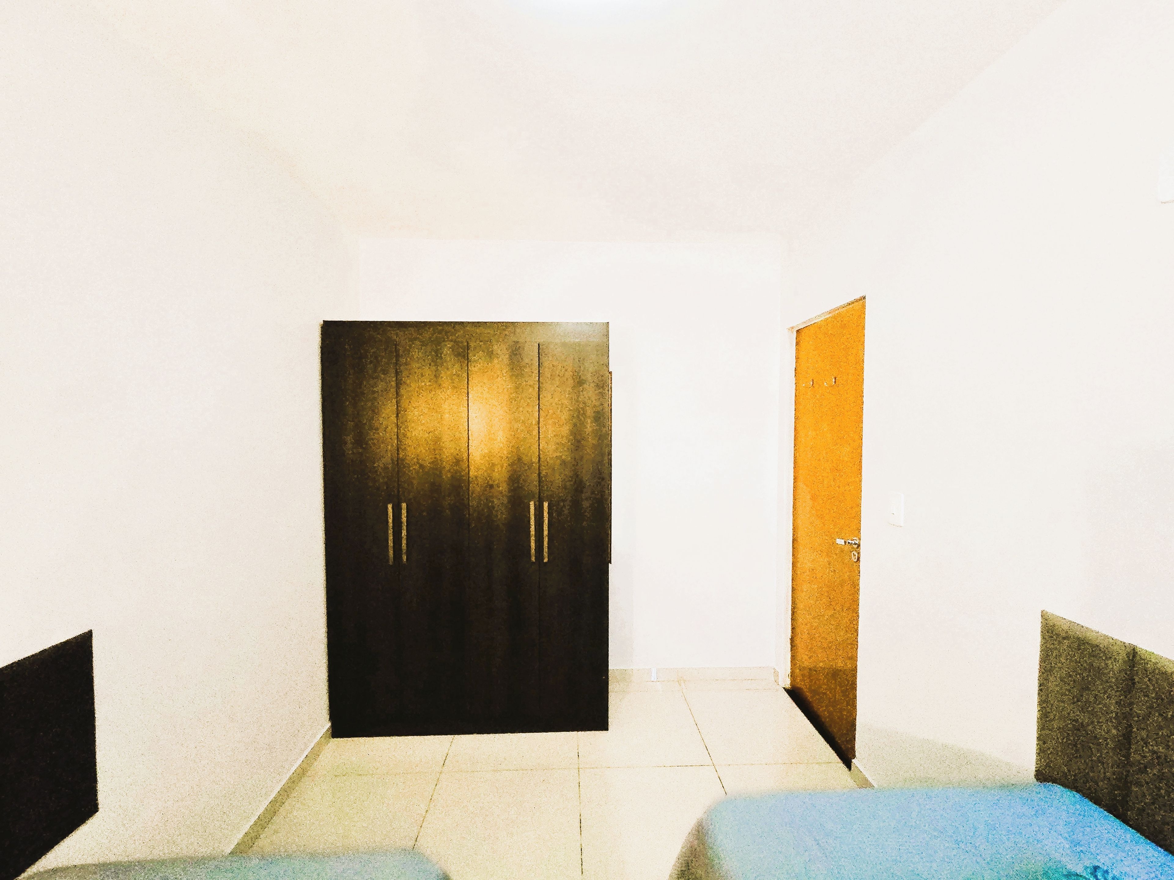 A room with a dark door, a light-colored floor, and a single bed.