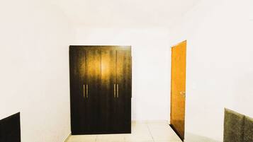 A room with a dark door, a light-colored floor, and a single bed.
