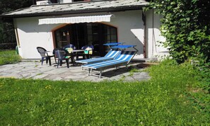 A small outdoor seating area with a table and chairs, a covered table, and two striped lounge chairs. - BRIGHT 2-BEDROOM CHALET-STYLE APARTMENT WITH PRIVATE GARDEN ACCESS (Zermatt)