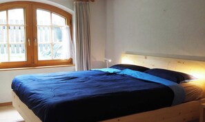 A bedroom with a wooden bed, a window with curtains, and a bedside lamp. - BRIGHT 2-BEDROOM CHALET-STYLE APARTMENT WITH PRIVATE GARDEN ACCESS (Zermatt)