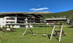 A traditional chalet with multiple balconies, a swing set, and a mountain backdrop. - BRIGHT 2-BEDROOM CHALET-STYLE APARTMENT WITH PRIVATE GARDEN ACCESS (Zermatt)