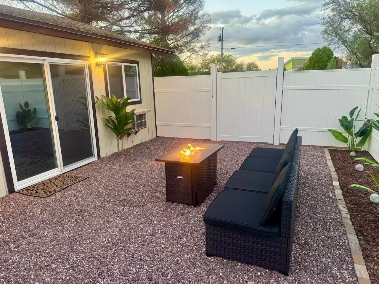 Un espace patio avec un foyer extérieur, des sièges de jardin et une clôture blanche.