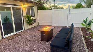 Un espace patio avec un foyer extérieur, des sièges de jardin et une clôture blanche.