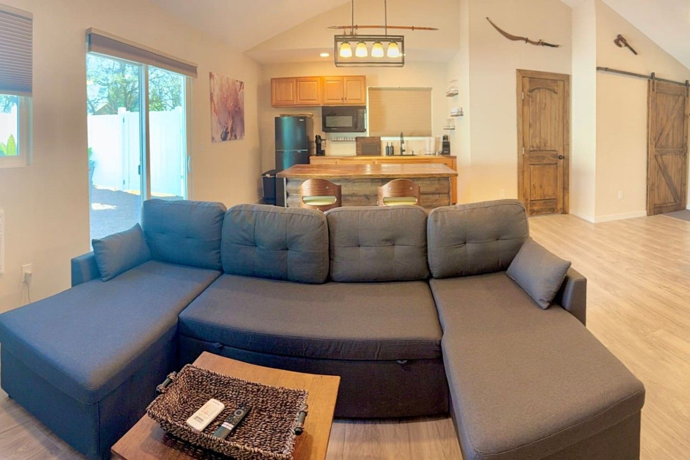 Un salon moderne avec un canapé d’angle, une cuisine en arrière-plan et une porte coulissante.