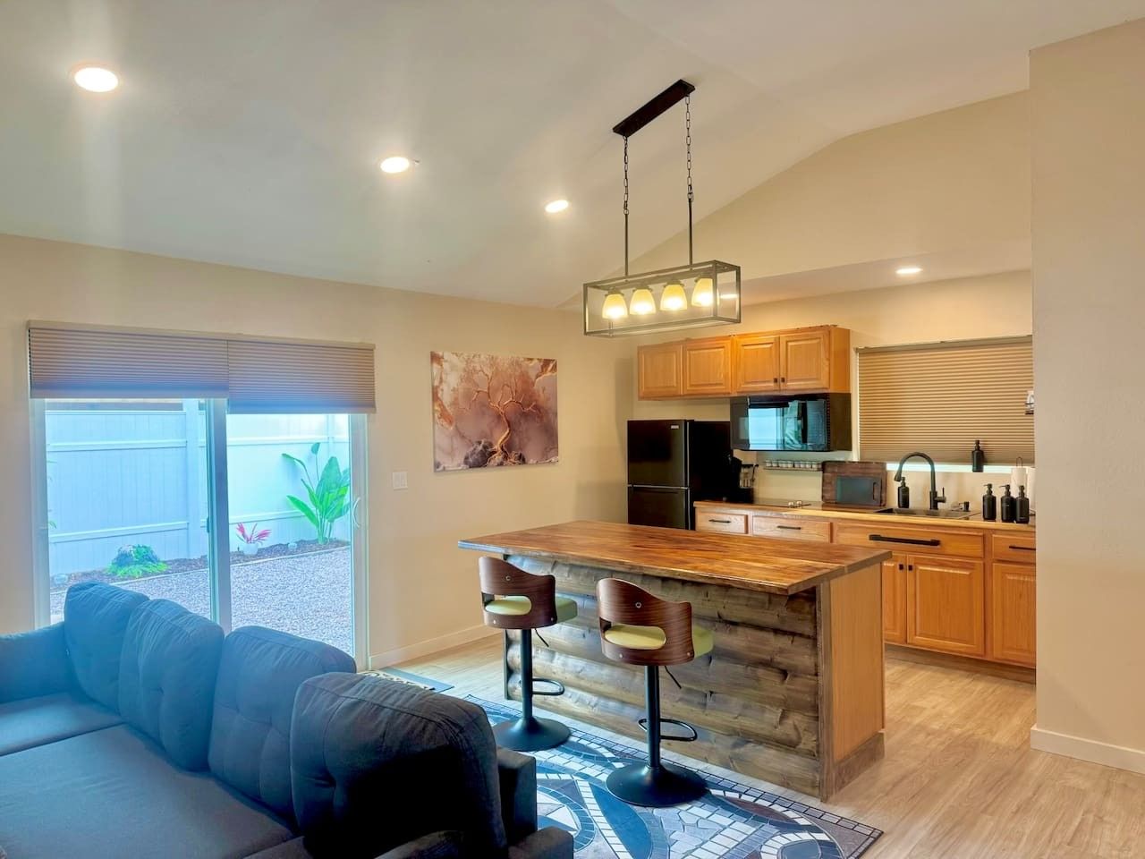 A modern kitchen with a bar area, wooden cabinets, and a dining space with a sofa.