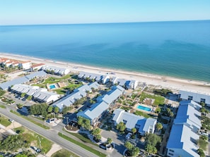 Ett flygbildsbild av ett hotell vid kusten med flera byggnader, en strand och en swimmingpool.