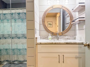 A bathroom with a round mirror, a sink, and a shower area with a patterned glass door. - New- Ocean Mile Retreat | Pet Friendly | 2 Pools (Saint George Island)