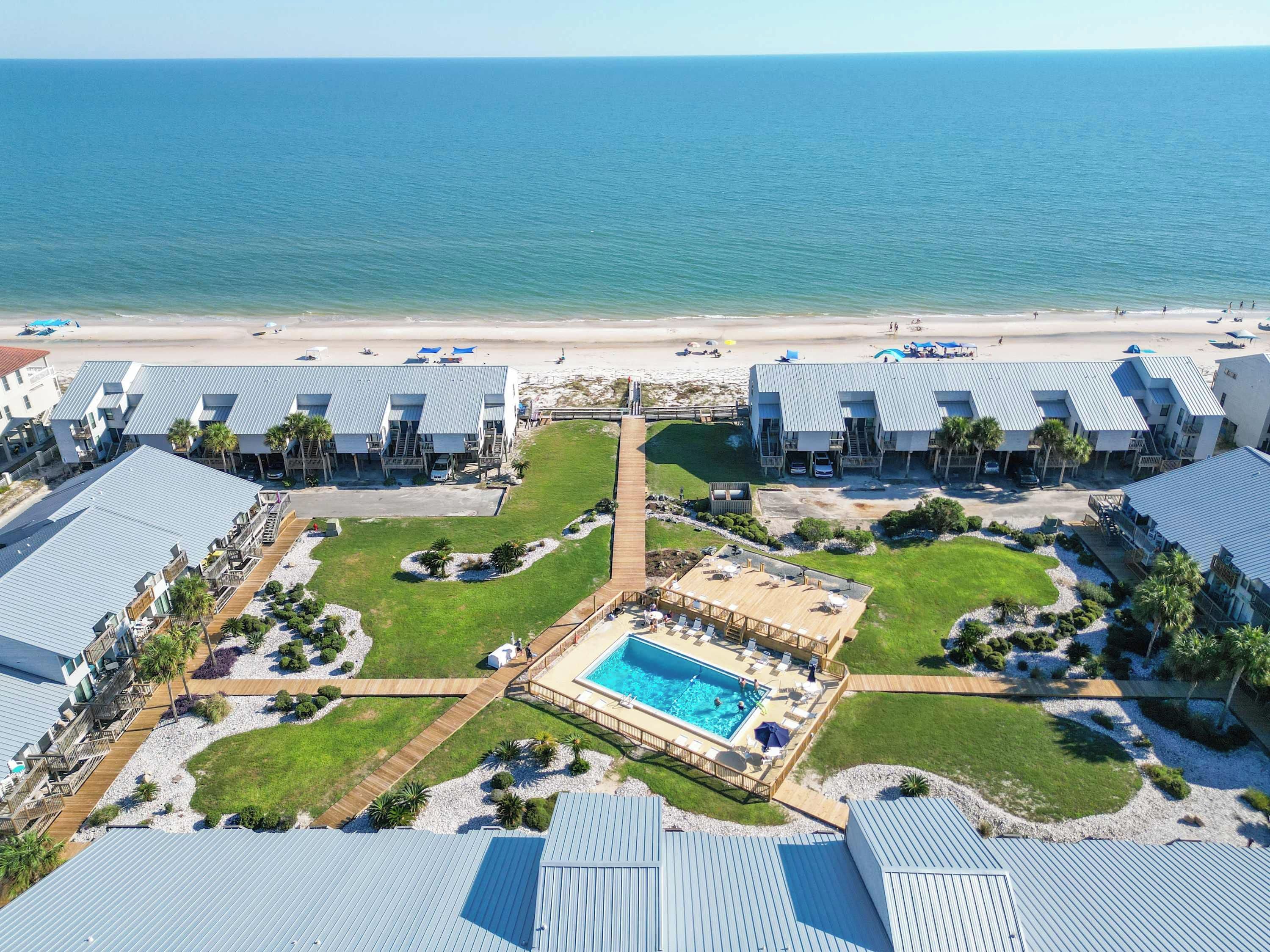 A resort with multiple buildings, a central pool, and a beach view.